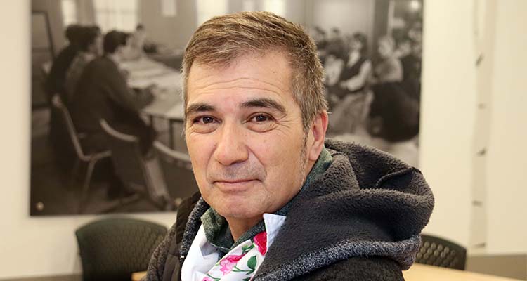 Robert Rayko, the cultural and community facilitator at Portage College sits in front of a wall-sized print depicting people at the 1970 sit-in protest that is an integral part in the history of Portage College and the community. 