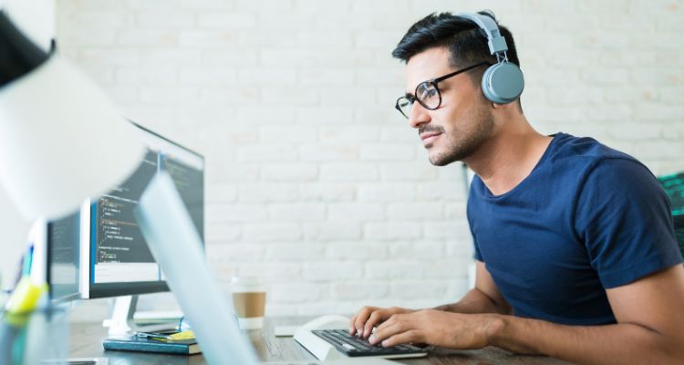 Man sitting at desk typing on a computer wearing headphones