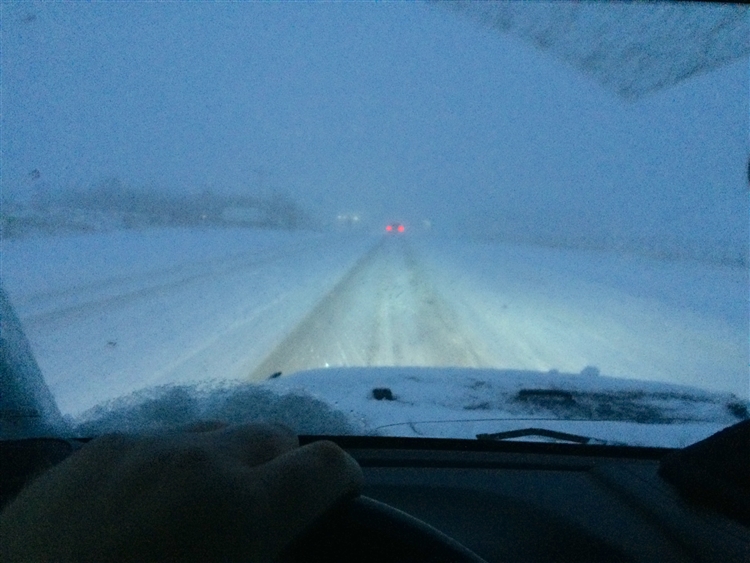 Image of a snowy, dark road taken from inside a parked vehicle