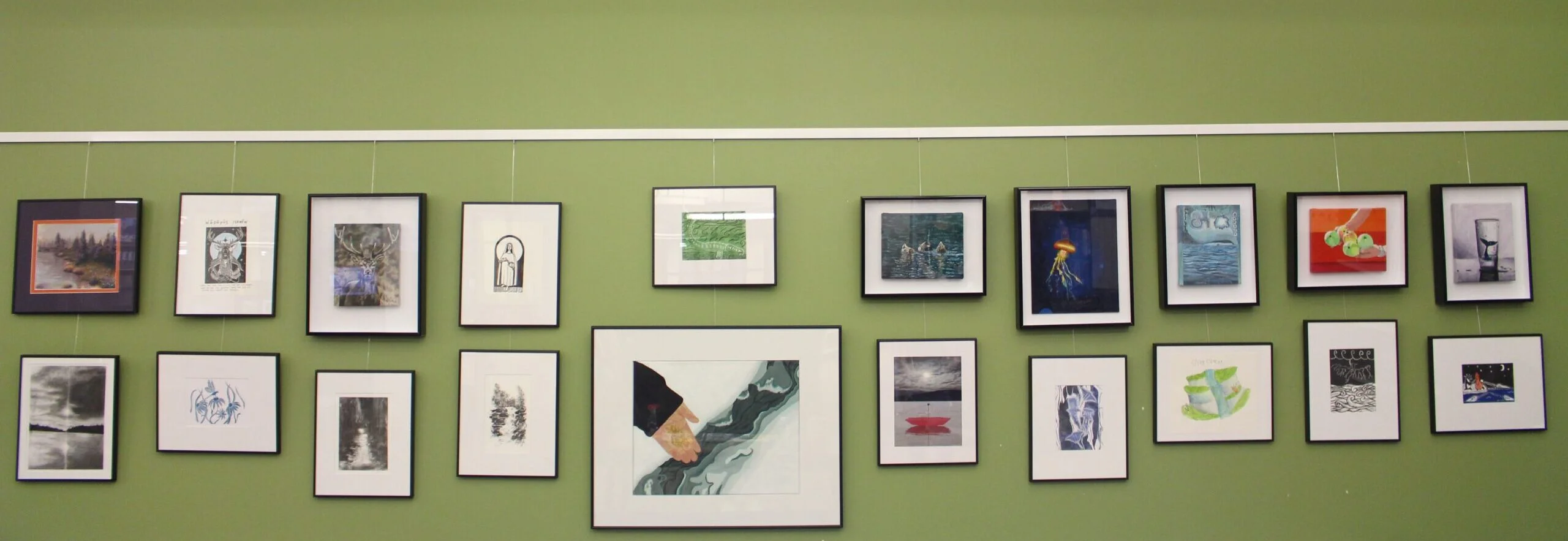 Edited display2 - Portage College Gallery wall with multiple small framed artworks arranged in a row on a green wall.