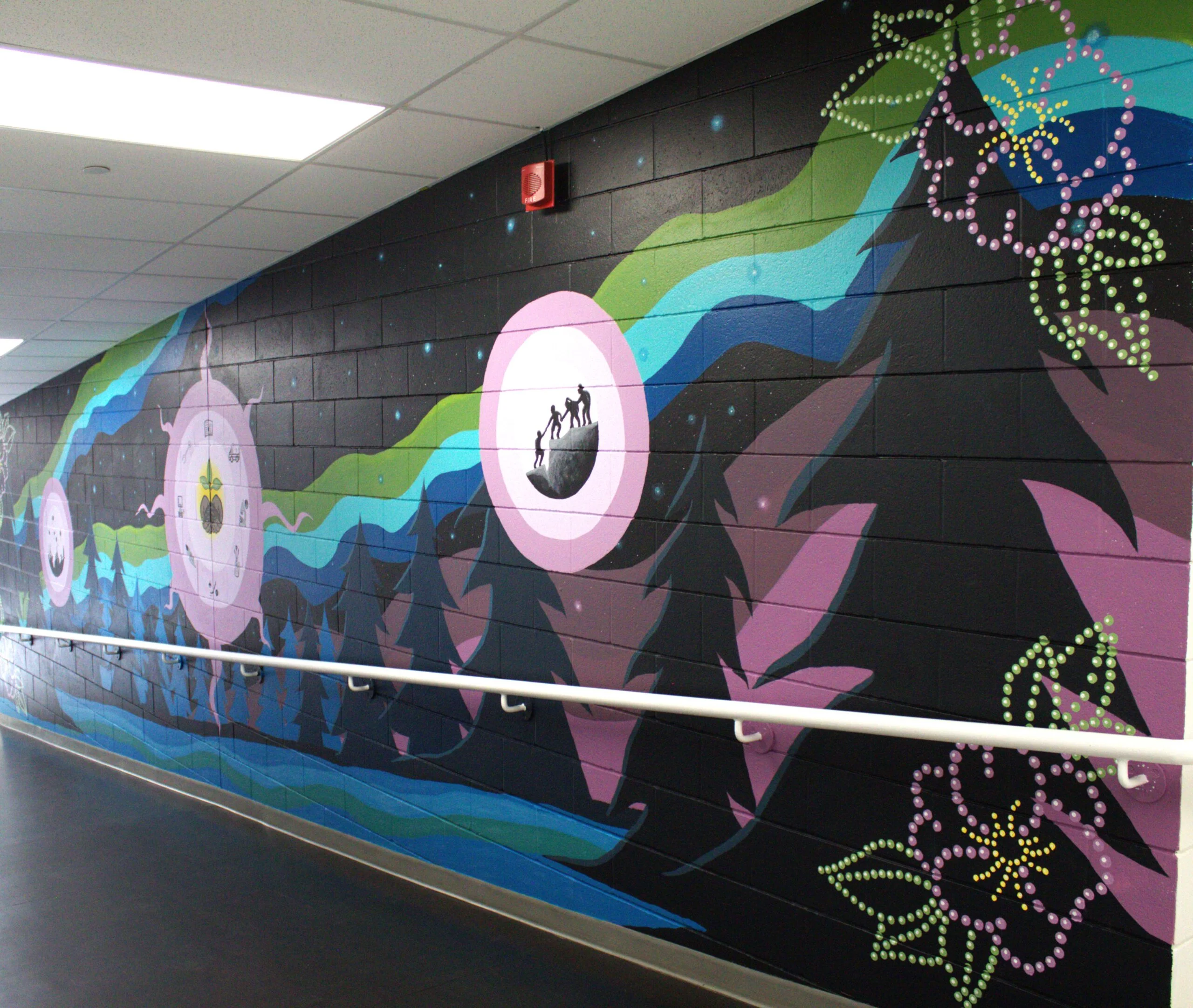 New Dawn - Portage College Indoor hallway with a colorful abstract mural featuring swirls and shapes; a red fire alarm is mounted on the wall above a white handrail.