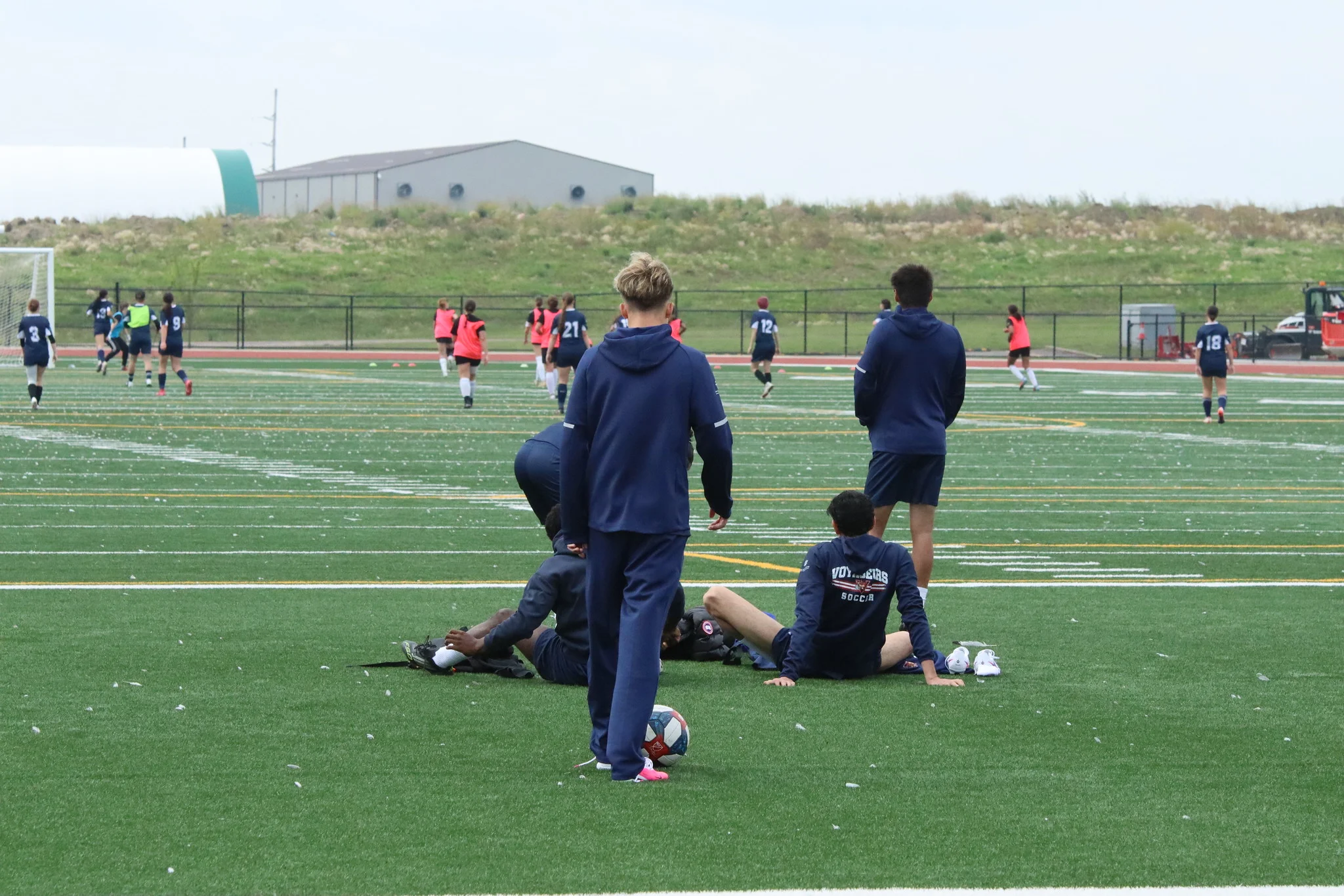 Youth soccer practice on an artificial turf field; players in dark uniforms and pink pinnies, with a ball in the foreground.